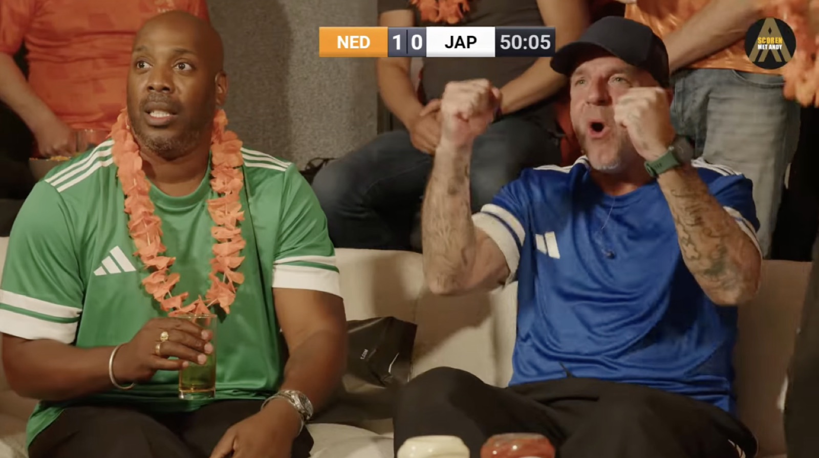 Kijkers juichen op de bank tijdens Nederland tegen Japan, met de stand in beeld